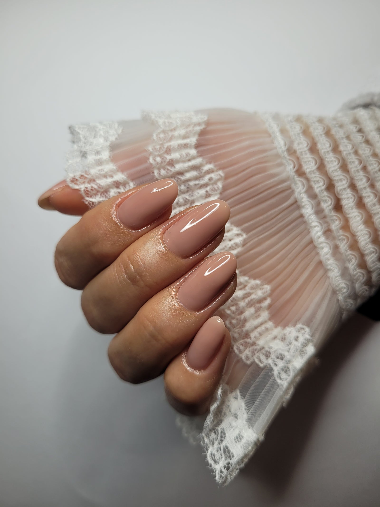 Nude amandelnagels tegen een kanten manchet